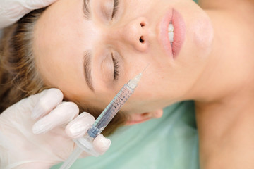 Cosmetologist making mesotherapy injection. Syringe and needle injecting botox. Female patient, woman is getting botox procedure at beautician. Hardware cosmetology, face rejuvenation.  Close up