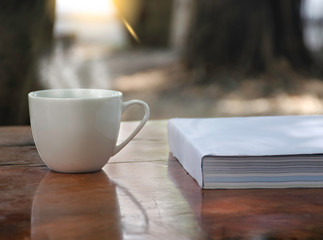Hot coffee mug placed on a white book in a wooden table On a green background