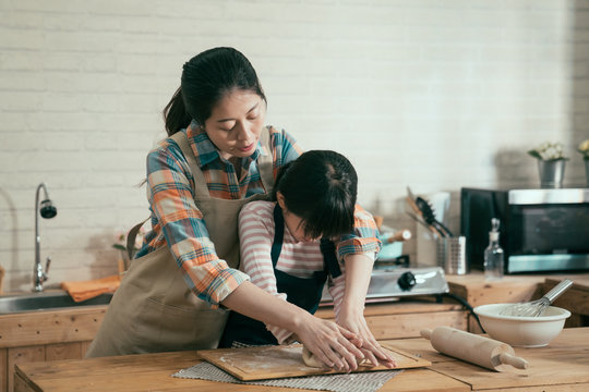 Little Girl Kneading Flour With Asian Mom On Mothers Day Handmade Cake For Easter. Young Woman In Apron Teaching Kid Baking Bread For Dad Birthday. Family Love Spending Time Together In Home Kitchen