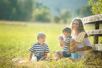 Young pretty mother having picnic with her little children. Family drinking milk outdoors