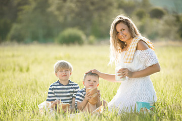 Young pretty mother having picnic with her little children. Family drinking milk outdoors