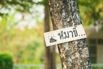 The wooden sign is hanging on the tree in foreign language (Thai Language) meaning "The dog poop zone" with drawing poop icon in natural green environment at public place.