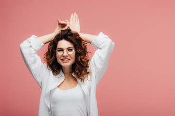 Fototapeta premium attractive curly woman in glasses smiling while gesturing on pink