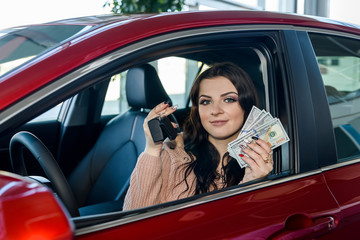 Woman sitting in new car and showing dollars and keys