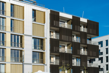 Hausfassaden von zwei Mehrfamilien-Wohnhäusern mit Balkonen und dunkelbrauner Holzverkleidung in Lamellenform im Wohngebiet Neckarbogen in Heilbronn am Neckar in Baden-Württemberg.