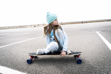 Fototapeta na wymiar Street sports: A girl in a blue sweater and cap quickly rolls on a longboard.