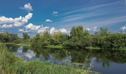 Naklejka na ściany i meble Beautiful summer landscape with pretty river and colorful trees. View of the sky with beautiful clouds. Stock photo