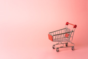 Red miniature trolley from a supermarket on a pink background. Close-up.