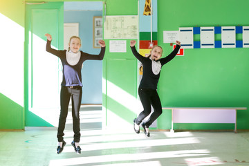 Fototapeta na wymiar Cheerful children jump in the school hallway. Two girls schoolgirls jump in height at school during the holidays