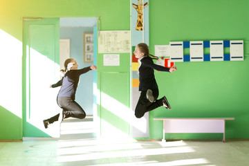 Fototapeta premium Cheerful children jump in the school hallway. Two girls schoolgirls jump in height at school during holidays.