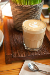 Hot cappucino cup place on wooden plate with spoon and napkin