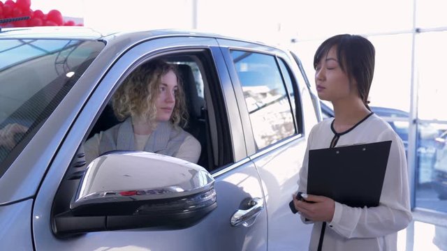 portrait of professional car seller hands over keys woman client inside vehicle while buying new automobile at dealership