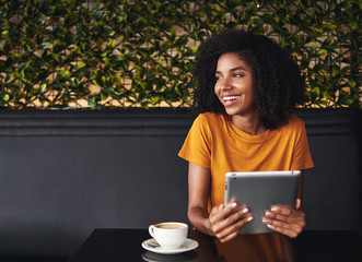 Happy young woman sitting in cafe holding digital tablet in hand