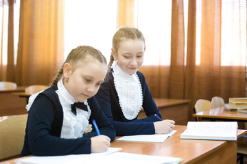 Girl classmate looks into someone else's notebook. The schoolgirl did not learn subject of the lesson at school and looks into someone else's notebook to write off the correct answer.