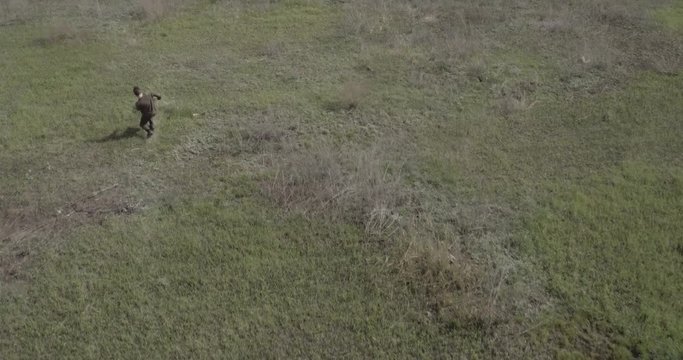 The guy is runing across the field and falling. Extreme wide shot. Drone