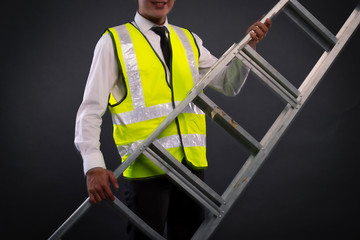 young technician or engineer holding alumminium ladder over dark background