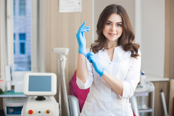 Yoyng beautiful doctor with copy space. Attractive dermatologist cosmetologist at the medical clinic. Beauty salon interior. Woman wearing uniform.