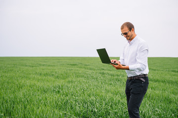 Young agronomist holds laptop in green wheat field. Agribusiness concept. agricultural engineer standing in a wheat field with a tablet in summer