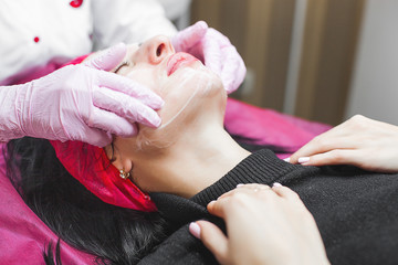 Cosmetologist making face care procedure. Specialist applying face mask to her client. Dermatology...