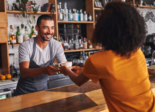 Male barista serves coffee cup to female customer in cafe