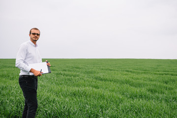 Young agronomist holds tablet touch pad computer in green wheat field. Agribusiness concept. agricultural engineer standing in a wheat field with a tablet in summer