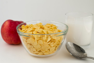 breakfast of corn flakes with milk and red apple, on white background