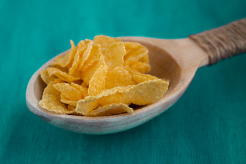 Cornflakes in a wooden spoon on a green background