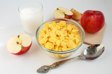 breakfast of corn flakes with milk and red apple, on white background