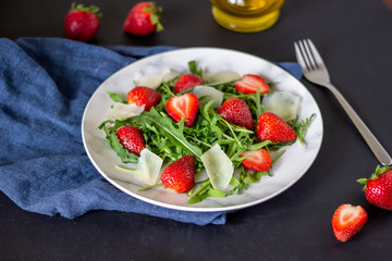 Salad of strawberries, arugula and cheese on a dark background. Dietary food.