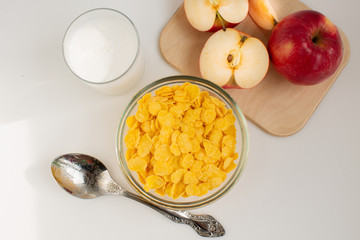 breakfast of corn flakes with milk and red apple, on white background