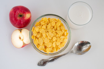  breakfast of corn flakes with milk and red apple, on white background