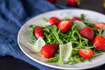Salad of strawberries, arugula and cheese on a dark background. Dietary food.