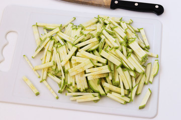 Zucchini sliced straws on a cutting board on a white background