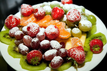 Obraz premium Ripe berries and fruit powdered with powdered sugar on a plate close-up