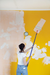 Woman painting with white paint over a yellow wall