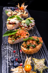 Tasty savory tomato Italian appetizers, or bruschetta, on slices of toasted baguette garnished with basil and avocado.