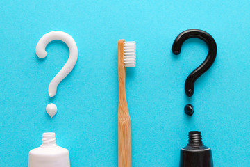 question from white and black toothpaste, teeth care concept, wooden toothbrush on blue background
