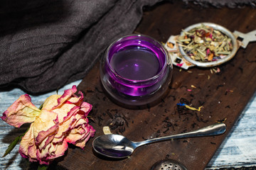 Tea in a transparent double glass with the addition of lemon becomes a gray color. A brown chalkboard next to a dry rose, a metal spoon and everything on a gray background. 