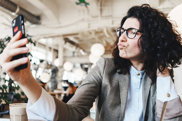 Joyful and fooling woman taking picture using mobile photo camera while sitting in city cafe