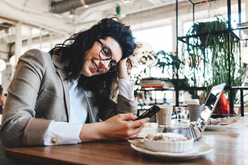Happy and handsome business lady sitting in city cafe with mobile phone