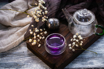Tea in a transparent double glass with the addition of lemon becomes a gray color. A brown chalkboard next to a dry rose, a metal spoon and everything on a gray background. 