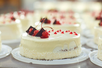 Obraz na płótnie Canvas Red cherry on white cake on a table with cakes