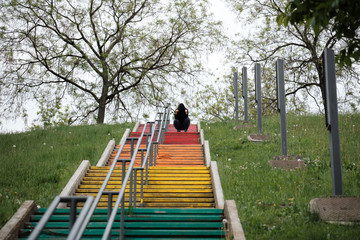 Fototapeta na wymiar woman fitness activity after workout girl doing rest and concentration in the park on colorful stairs with her head covered with a hood sweatshirt