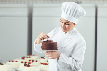 Confectioner decorating chocolate cake in pastry shop.
