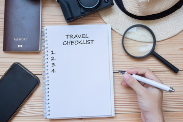 hand traveler writing Travel Checklist word on notebook with accessories, Camera, Passport,...