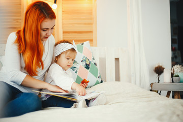 Obraz na płótnie Canvas Beatuful ginger mother playing with daughter. Little girl sitting on a bed at home. Family reading the book