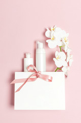 Cosmetics SPA branding mock-up. Flat lay top view White cosmetic bottle containers gift bag White Phalaenopsis orchid flowers on pink background. Natural organic beauty product concept