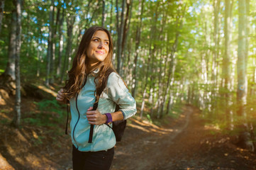 Young woman taking a walk in the forest, carrying a backpack in the forest on sunset light in the autumn season.