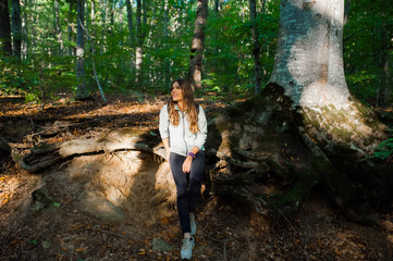 Young woman taking a walk in the forest, carrying a backpack in the forest on sunset light in the autumn season.