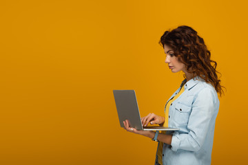 beautiful curly redhead girl using laptop on orange